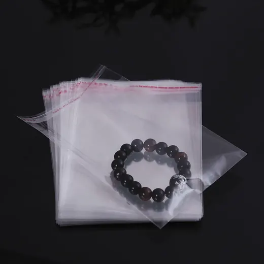 Stack of clear self-adhesive plastic bags with a dark beaded bracelet inside