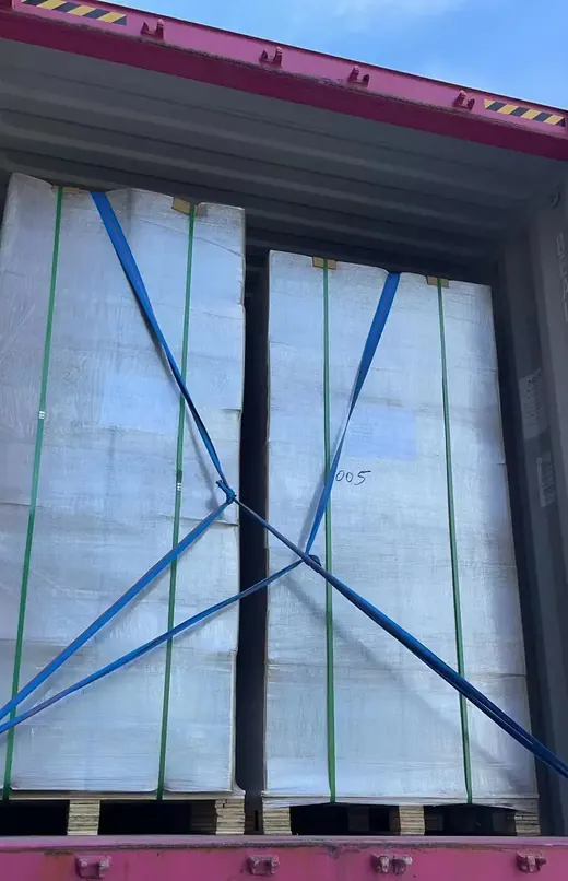 Large wrapped cargo bundles on pallets secured with blue and green lashing straps inside a shipping container