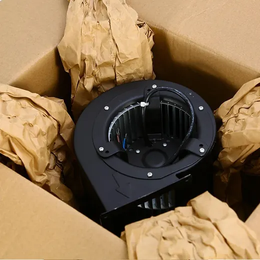 A black centrifugal blower fan nestled inside a cardboard box with crumpled brown paper.