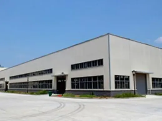 Exterior of a large white industrial factory building with rows of windows and loading doors under a clear blue sky