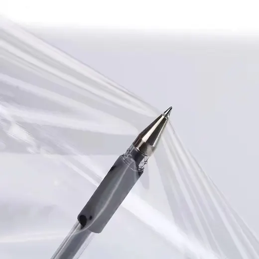 A close-up of a black pen tip pressing against a thin, transparent plastic film sheet.