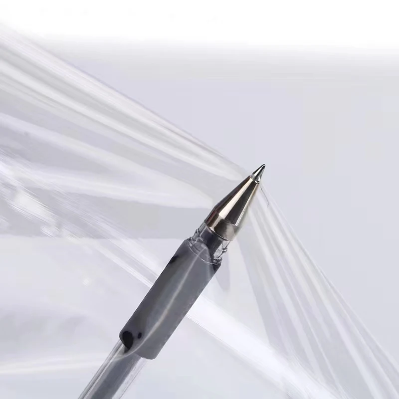 A close-up of a black pen tip pressing against a thin, transparent plastic film sheet.