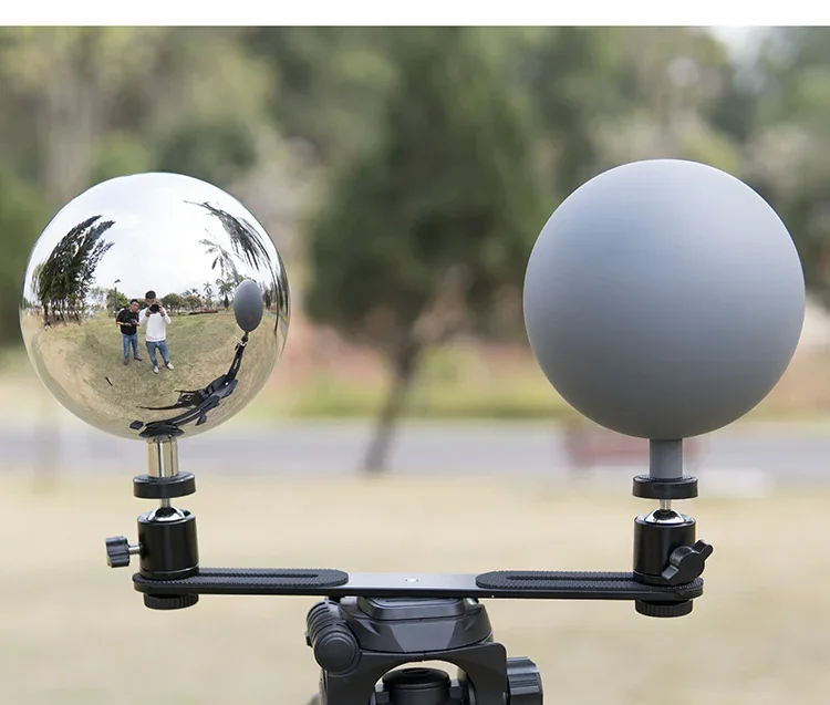 A polished chrome sphere and a matte gray sphere mounted on a tripod outdoors.