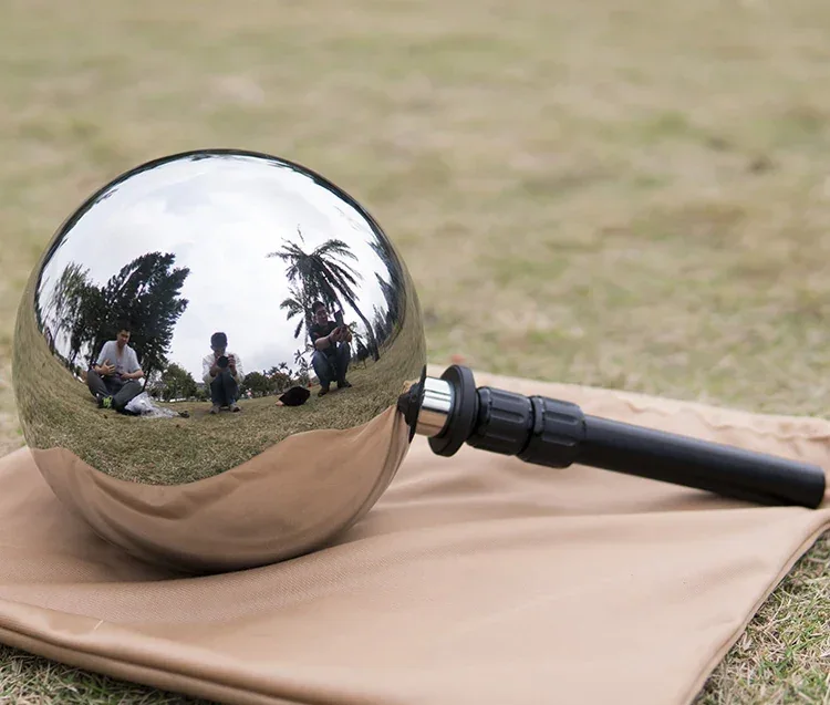 A polished metal bocce ball with a black handle resting on a beige bag outdoors