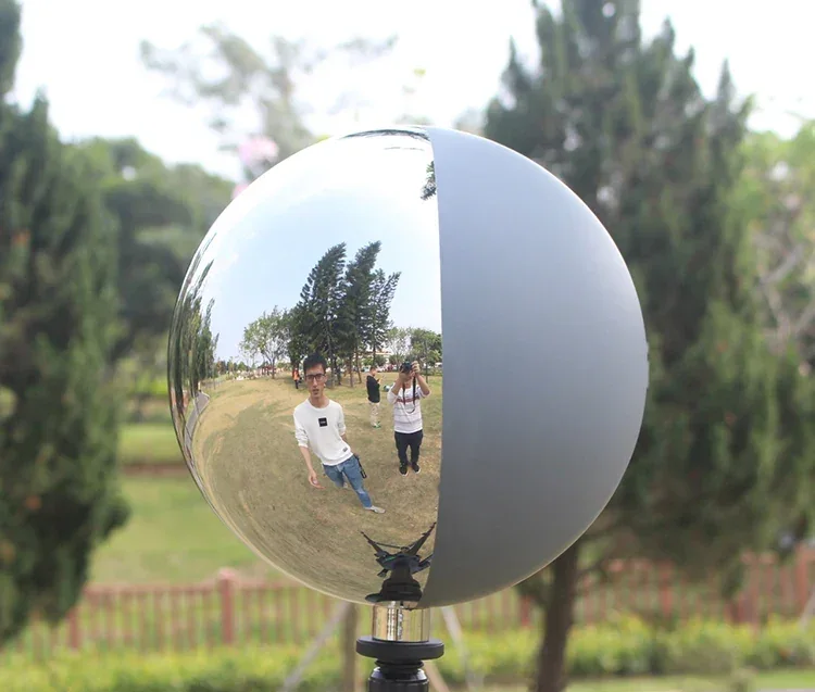 A polished metal sphere on a stand, reflecting two people taking a photo in a park.