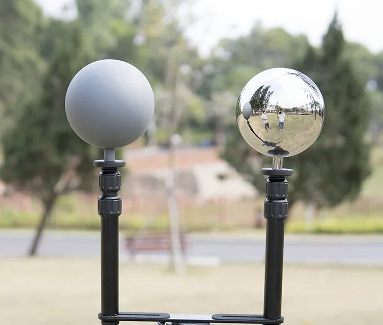 Two spherical weather station sensors, one gray and one chrome, mounted on black poles outdoors.