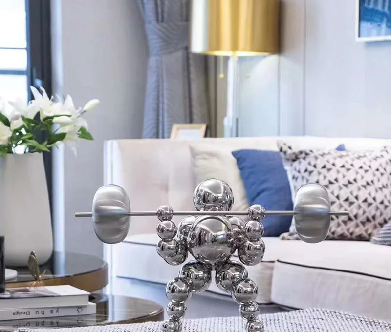Polished chrome sphere figurine posed lifting a barbell, displayed on a table in a styled living room