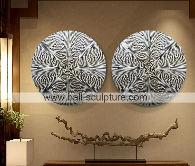 Two round textured silver metal wall art discs mounted on a beige wall above a driftwood sculpture on a stand