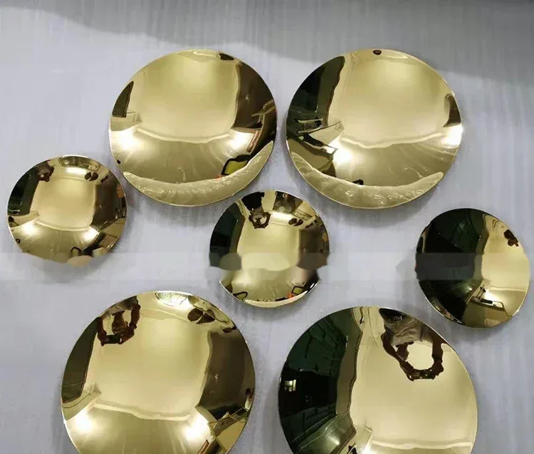 Polished gold-colored metal hemispheres of various sizes arranged on a white fabric surface