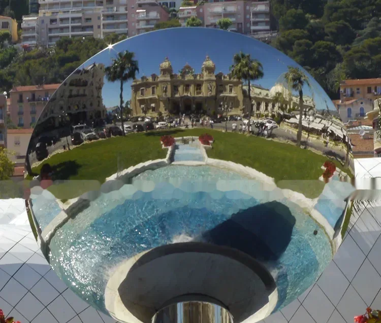 Large mirrored sphere reflecting a grand building, palm trees, garden pool, and hillside city buildings