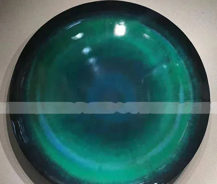 Large ceramic plate with glossy green and teal glaze displayed on a light wall