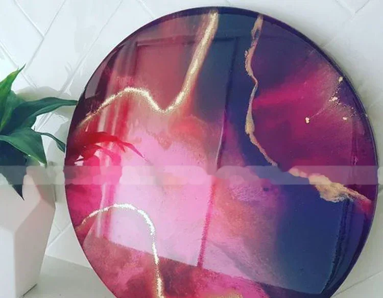 Round pink and purple abstract resin wall art with gold accents leaning against a white tiled wall.