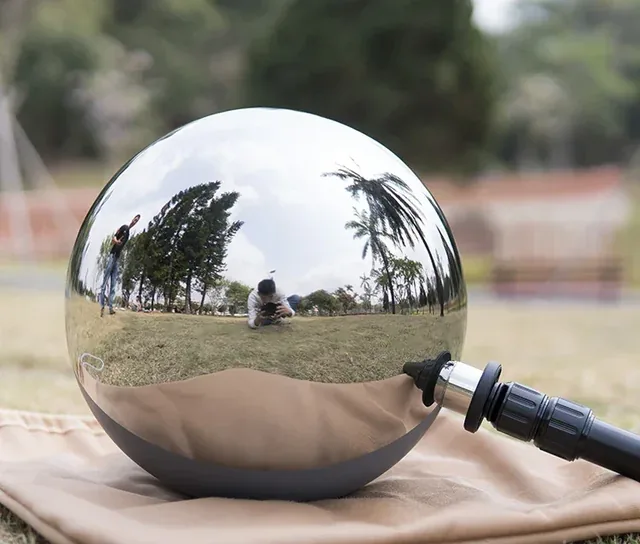 A highly polished, reflective stainless steel sphere resting on a cloth outdoors.