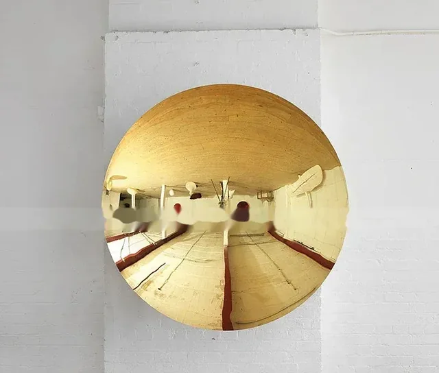 Round golden convex mirror mounted on a white brick wall reflecting an interior room