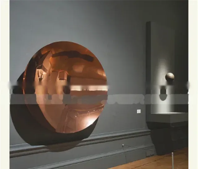 A large circular copper-colored disc mounted on a grey wall in an art gallery.