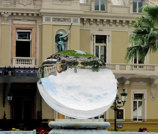 Large mirrored sphere sculpture reflecting an ornate building and palm tree in a city plaza