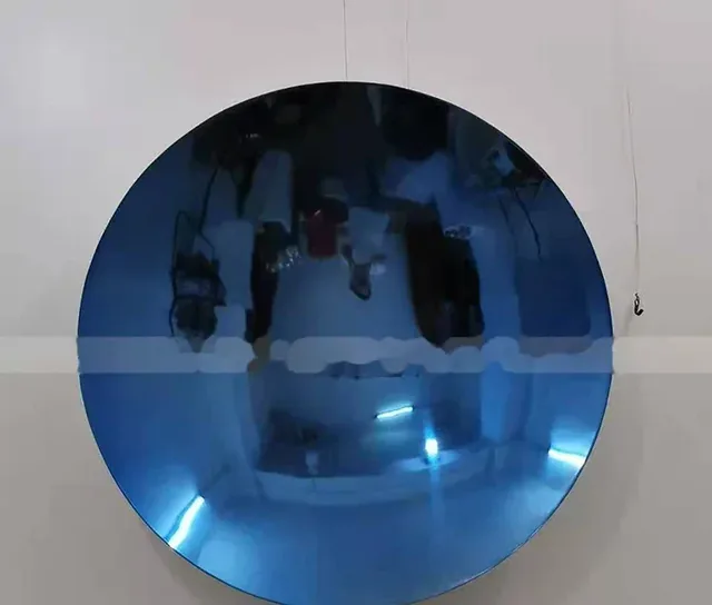 A circular, polished metal disc with a blue tint reflects the photographer and room lights.