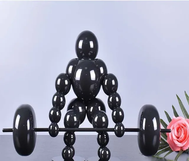 Glossy black figurine of a weightlifter made of spheres lifting a barbell, pink rose beside it