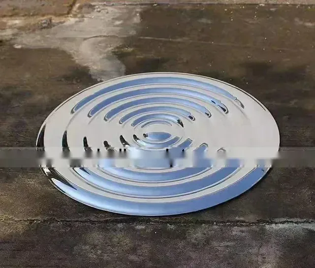 Polished stainless steel disc sculpture with concentric ripple grooves resting on concrete ground