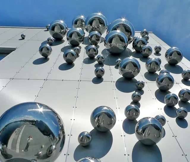 Polished stainless steel spheres of various sizes mounted on a metallic building facade against a blue sky