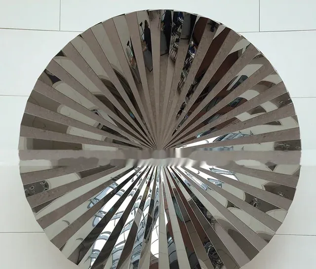 Circular polished metal sculpture with radial slats reflecting the environment.
