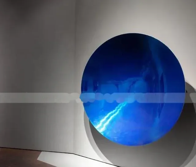 A circular blue artwork mounted on a gray wall casting a shadow.