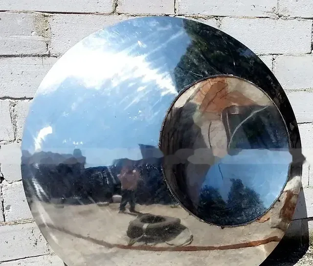 Large polished stainless steel sphere with circular opening leaning against a white brick wall