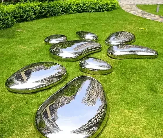 Several polished stainless steel sculptures shaped like smooth stones arranged on a green lawn.