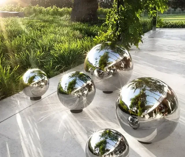 Several polished stainless steel spheres of varying sizes arranged on a stone walkway in a park.