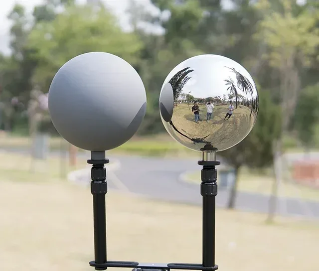 Side-by-side comparison of a matte grey sphere and a polished chrome sphere mounted on stands outdoors.