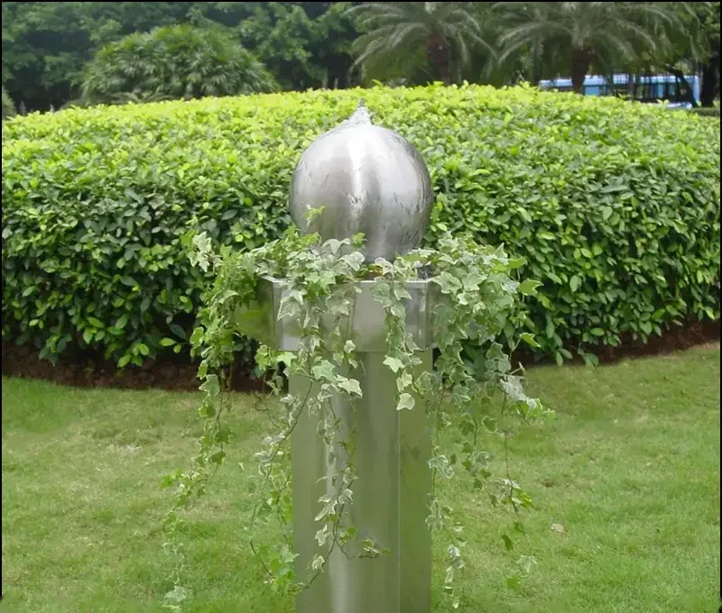Stainless steel sphere water feature with trailing ivy on a metal pedestal in a grassy garden