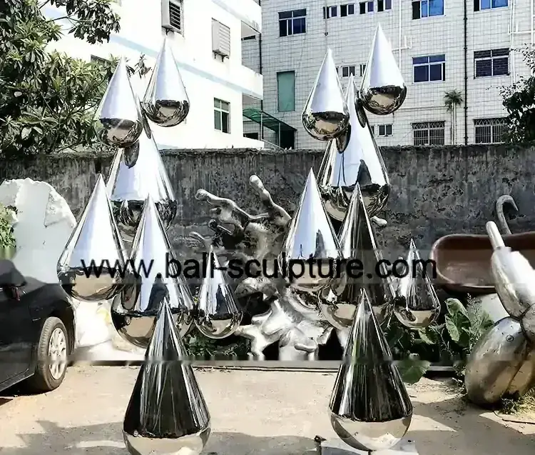 Cluster of polished stainless steel teardrop-shaped sculptures with mirrored surfaces in an outdoor yard