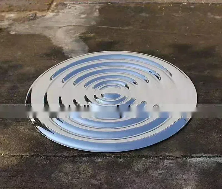 Polished stainless steel disc sculpture with concentric ripple grooves resting on concrete ground
