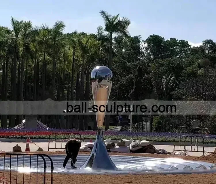 Large reflective steel sculpture standing in an outdoor park setting.