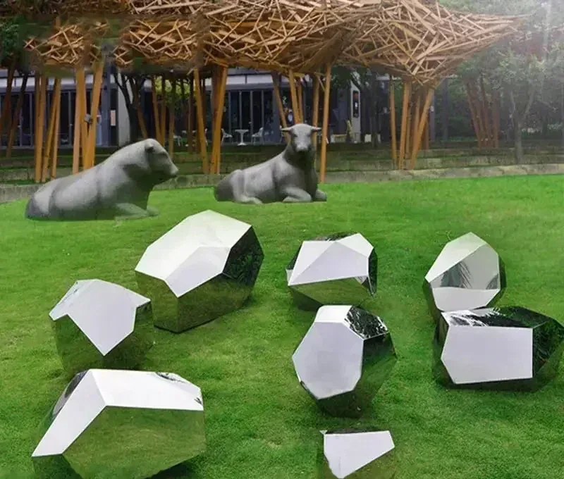 Outdoor park featuring metallic geometric sculptures on green turf and stone animal statues.