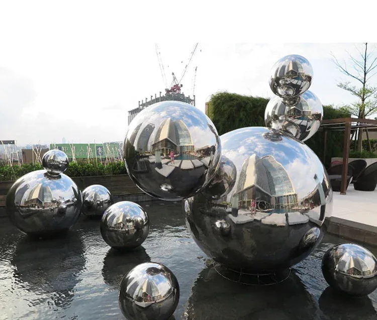 Polished stainless steel spheres of various sizes arranged in and around an outdoor water feature