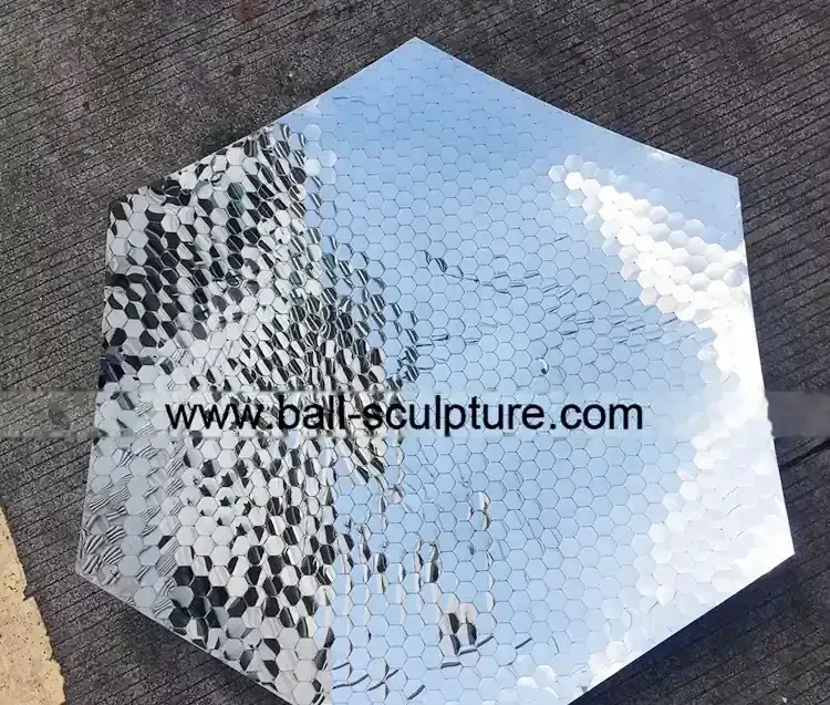 Hexagonal mirror-polished stainless steel panel with dimpled honeycomb texture lying on concrete ground