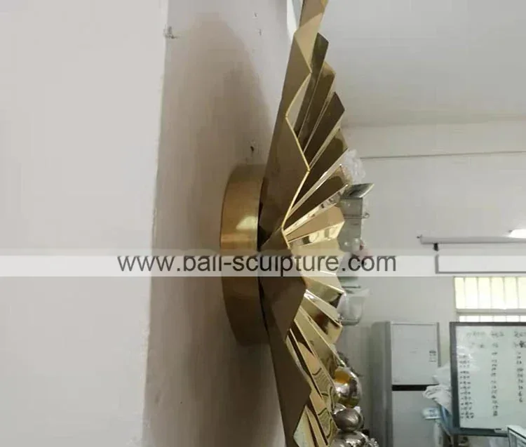 Polished gold fan-shaped metal wall sculpture mounted on a white wall, photographed in a cluttered workshop
