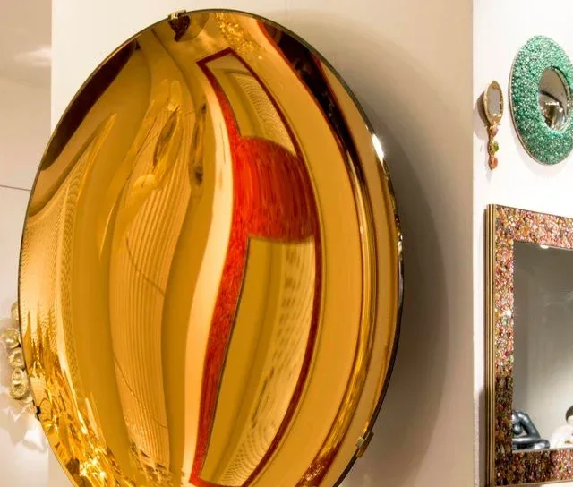 A large, round gold convex mirror mounted on a wall, reflecting a red chair and room interior.