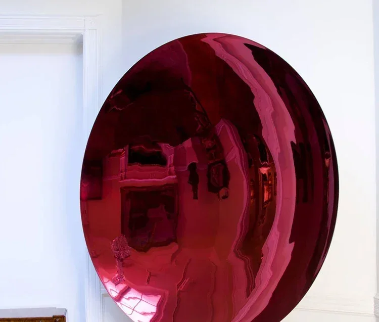 Large polished red metallic sphere sculpture reflecting a white gallery room