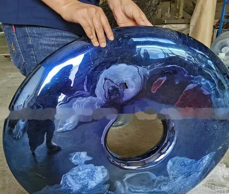 A person holding a large, glossy blue toroidal sculpture with a central hole.