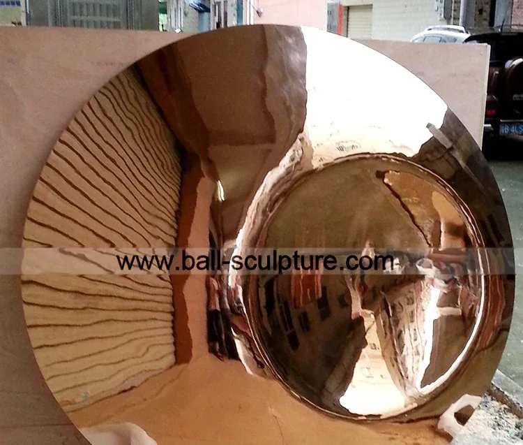 Large polished gold-toned hemispherical metal dish, a sculpture component, photographed outdoors with a truck and workshop behind