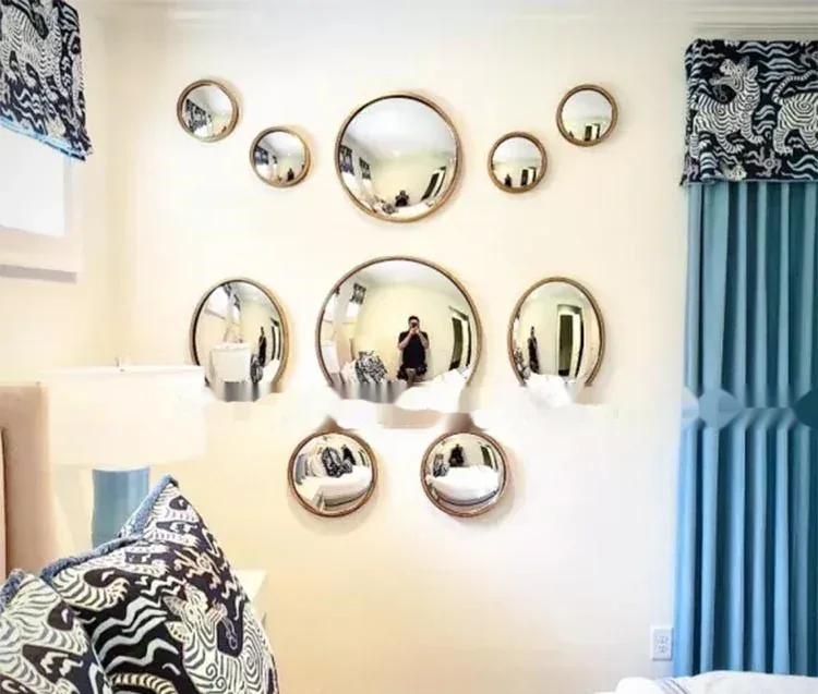 Assorted round decorative mirrors in various sizes mounted on a bedroom wall with blue curtains
