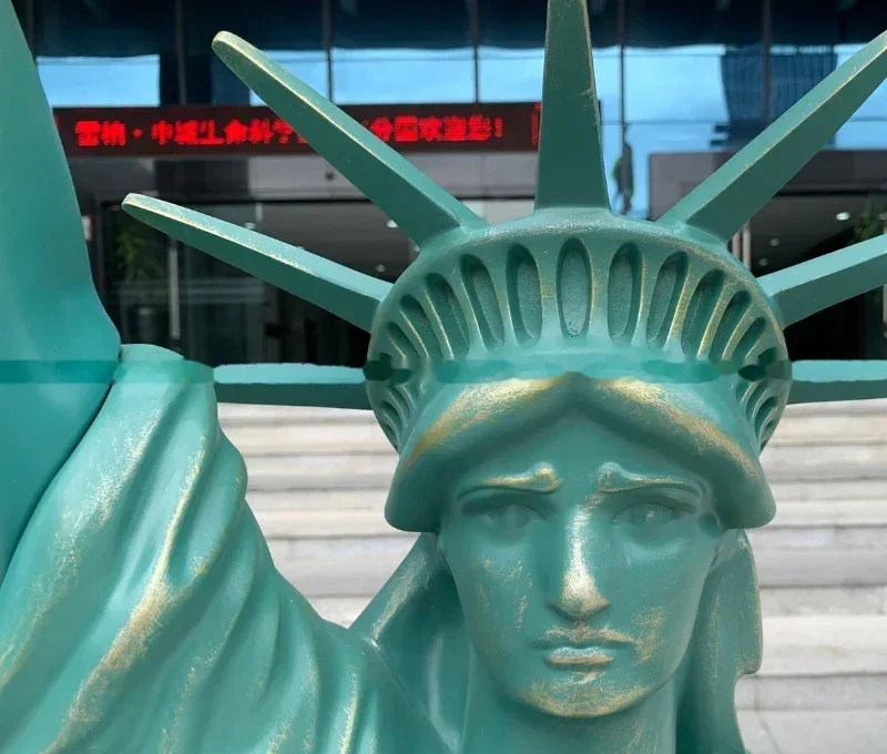 Close up of a green Statue of Liberty replica with a red LED sign in the background