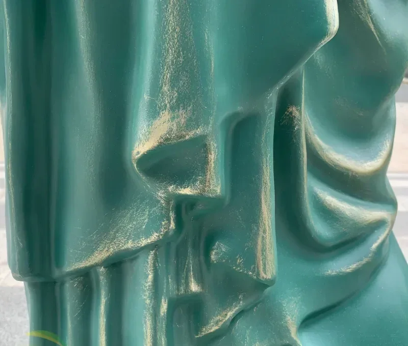 Extreme close-up of a teal-green patinated sculpture with draped, fabric-like folds and gold accents