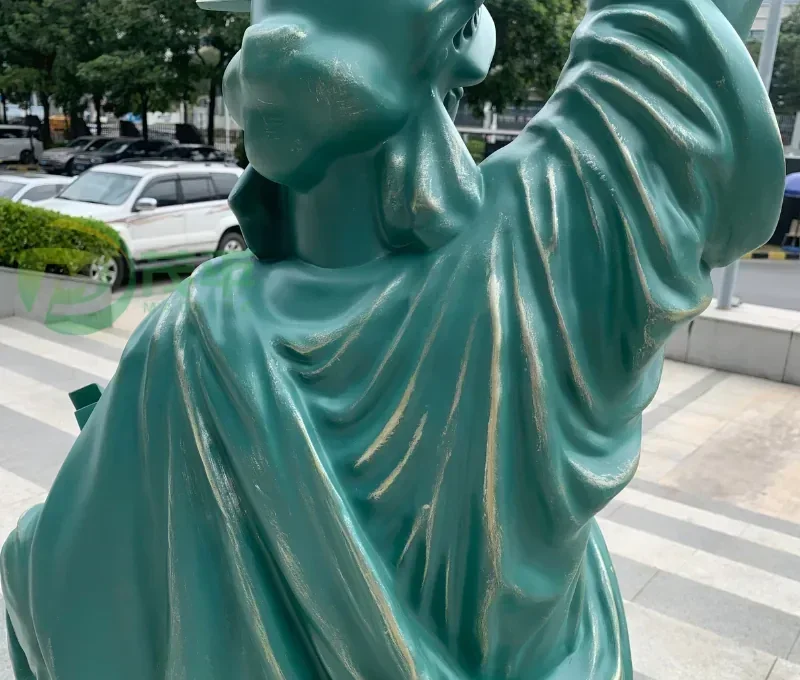 Close up of a green statue of a figure with raised arm on a city street.