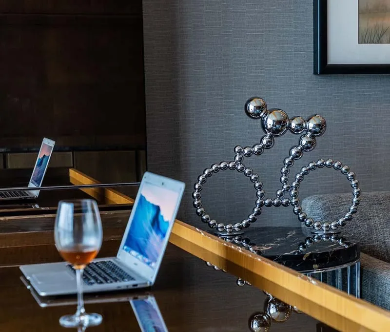 A chrome bicycle sculpture made of balls sits on a table behind an open laptop and a glass of wine.