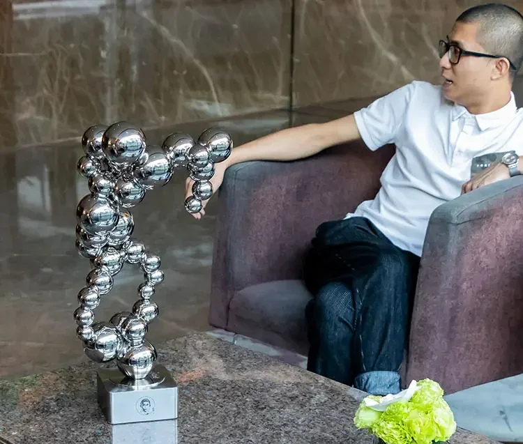 Man sitting on armchair next to abstract metal sphere sculpture on table