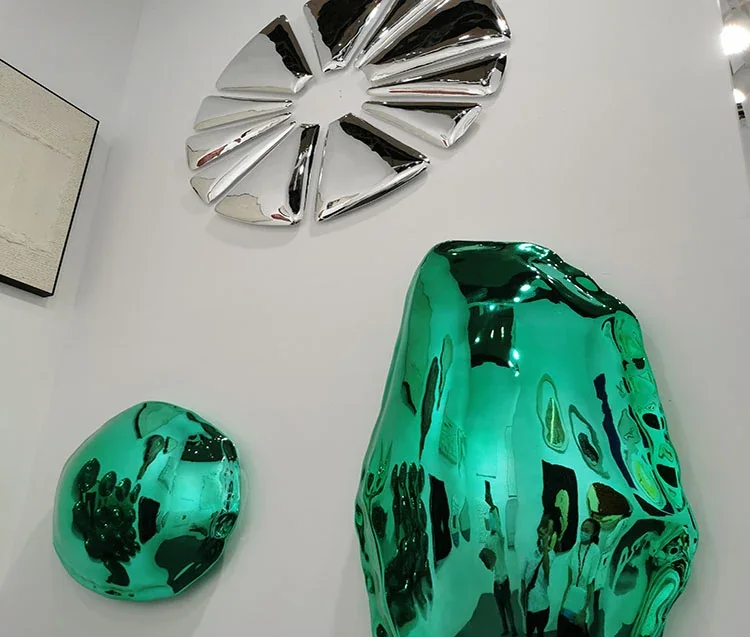 Glossy teal rock-shaped sculptures and a chrome starburst wall piece in an art gallery