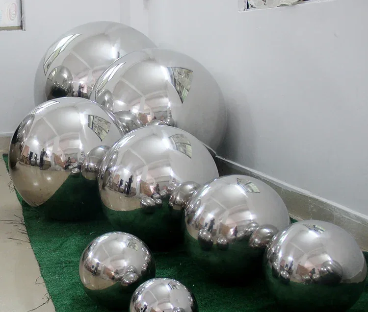 Multiple polished mirror-finish stainless steel spheres of various sizes arranged on green artificial turf flooring